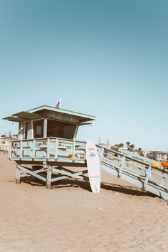 a lifeguard station on the beach with a surfboard leaning against it's fence