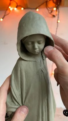 a hand holding a clay statue of a person with a hood over it's head