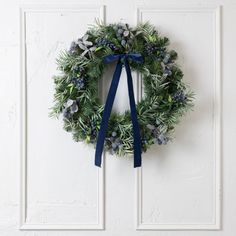 a wreath hanging on the front door of a house with blue ribbon tied around it