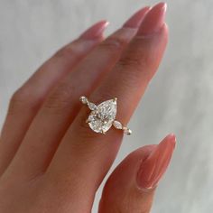 a woman's hand holding an engagement ring with a pear shaped diamond on it