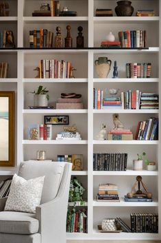 a living room filled with lots of white bookshelves next to a gray couch