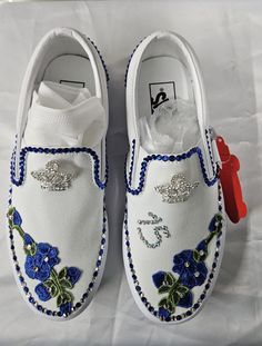 a pair of white shoes with blue and green flowers on the side, one has a red shoe clip