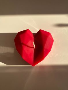 a red heart shaped origami piece on a white surface with the shadow cast by it