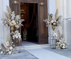 an entrance to a building decorated with flowers and greenery in gold vases on pedestals