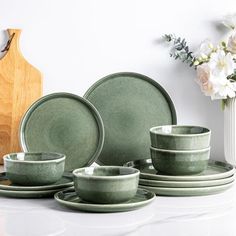 a set of green dinnerware on a white countertop with flowers in the background