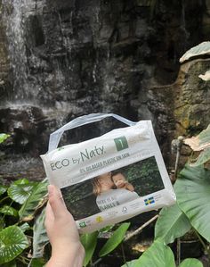 a person holding up a bag with an image of a woman on it in front of a waterfall