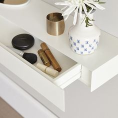 a white vase with flowers and makeup brushes in it on top of a table next to a mirror