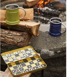 two mugs sitting on top of a table next to a fire pit and logs