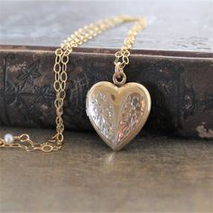 This vintage locket is engraved with a floral design on the front; the reverse is plain.  The heartshaped pendant opens revealing two compartments in which to place your favorite photos.  The locket hangs from a new 14k gold filled textured chain accented with tiny pearls the clasp.    ★Personalize the locket with our charms:https://www.etsy.com/shop/lexiandgem?section_id=6307004Locket 24x20mmNecklace length 18" (45cm)✦All of our vintage lockets ship with complimentary insurance✦✤Our entire sele Gold Heart Locket Necklace, Locket Gold, Push Present, Gold Heart Locket, Gold Locket Necklace, Vintage Locket, Wedding Jewelry For Bride, Picture Locket, Heart Locket Necklace