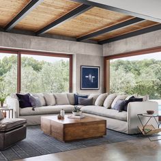 a living room filled with lots of furniture next to large windows and wooden ceiling beams