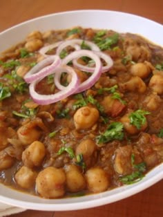 a white bowl filled with beans and onions on top of a wooden table next to a fork