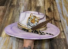 ✨THIS IS A CUSTOM HAT BAND ONLY✨ Made to fit most hats with a tie closure.  One of a kind purple and gold band with gold metallic tipped feather & unique pin to cheer on our Tigers in one of a kind style!!  ⭐️Please Note: Creating your order may take 10 to 14 days from the time your order is placed before it ships. ⭐️ Photos are examples that have been previously made. These are made to order. All bands, buttons, overall distressed look may vary slightly, since these are all one-of-a-kind pieces Adjustable Purple Top Hat With Curved Brim, Adjustable Gold Fedora For Festivals, Purple Adjustable Hat For Kentucky Derby, Adjustable Purple Hat For Kentucky Derby, Fedora Hat Bands For Kentucky Derby Gift, Adjustable Gold Fedora For Kentucky Derby, Adjustable Wide Brim Top Hat As Gift, Adjustable Wide Brim Purple Mini Hat, Adjustable Wide Brim Purple Fedora