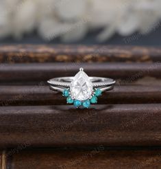 an engagement ring with turquoise stones and a pear shaped diamond on the side, sitting on top of a wooden table