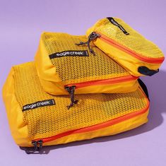 two yellow bags sitting on top of each other in front of a purple background with orange zippers