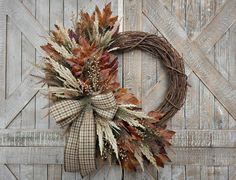 a wreath is hanging on the side of a barn door decorated with dried leaves and grass