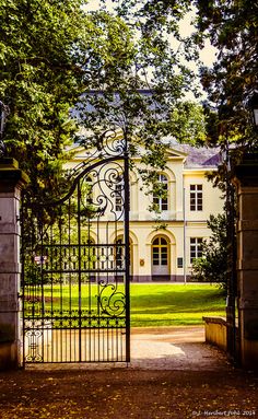 an iron gate in front of a large white building with trees on both sides and a walkway leading to it