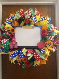 a colorful wreath is hanging on the door with a white board in it's center