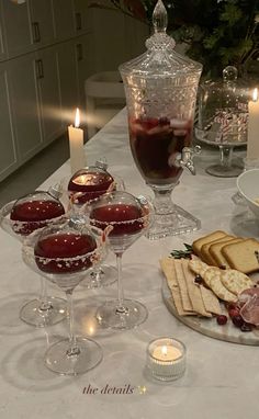 a table topped with wine glasses filled with desserts and crackers next to candles