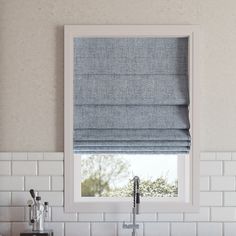 a kitchen sink under a window covered in blue roman shades