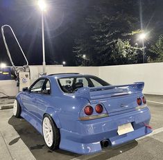 a blue sports car parked in a parking lot at night with its hood up and lights on