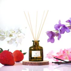 a candle, strawberries, and flowers on a table next to a bottle of reeds