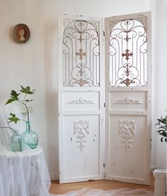 two white doors are open in a room with a table and vase on the floor