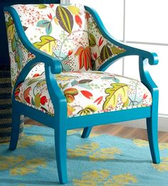 a blue chair sitting in front of a window next to a vase with flowers on it