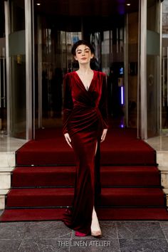 a woman in a long red dress standing on steps with her hands behind her back