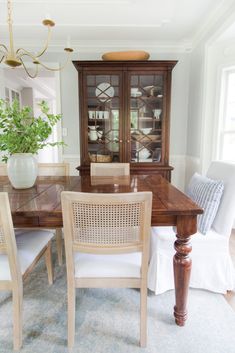 a dining room table with chairs and a china cabinet in the corner, along with a potted plant