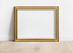 an empty gold frame on the floor in front of a white wall with a wooden floor