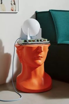 an orange mannequin head with a light on it's head, next to a green couch