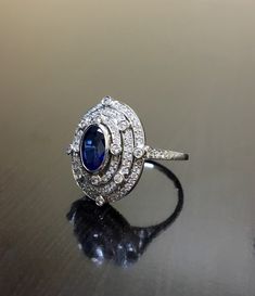 DeKara Designs Collection Art Deco Inspired Extremely Elegant Halo Sapphire Diamond Engagement Ring. Metal- 90% Platinum, 10% Iridium. Stones- 1 Oval Ceylon Blue Sapphire 1.25 Carats, 100 Round Diamonds F-G Color VS2 Clarity .80 Carats. Size- 6 1/4. An Amazing Art Deco Inspired Ceylon Blue Sapphire Triple Halo Diamond Engagement. The ring features a beautiful Ceylon Blue Sapphire that is expertly bezel set in the center. The sapphire is surrounded by 92 pave and burnish set round sparkling diamo Luxury Sapphire-colored Diamond Ring With Diamond Cut, Luxury Sapphire-colored Diamond Ring, Art Deco Diamond Ring With Gemstone, Exquisite Diamond-cut Sapphire Ring, Exquisite Diamond Cut Sapphire Ring, Luxury Oval Diamond Cut Sapphire Ring, Art Deco White Gold Halo Ring, White Gold Art Deco Halo Ring, Exquisite Diamond Ring With Polished Finish