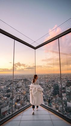 a woman in white robe standing on top of a building looking out at the city