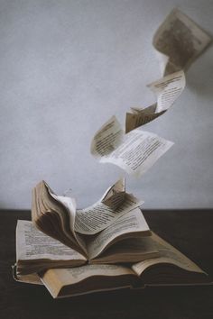 an open book flying through the air with pages falling off it's back end