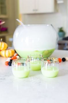 four glasses sitting on top of a counter next to a bowl and other items in the background