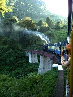 a blue train traveling over a bridge next to lush green mountains