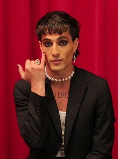 a woman in a suit and pearls holding her hand up to her face while posing for the camera