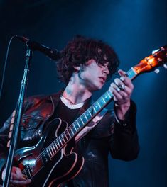 a man holding a guitar while standing in front of a microphone