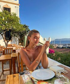 a beautiful woman sitting at a table in front of a building with an ocean view