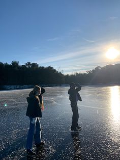 two people are standing on an ice covered lake with the sun shining behind them and trees in the distance