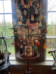 a small christmas tree with ornaments on it in front of a window and rocking chairs