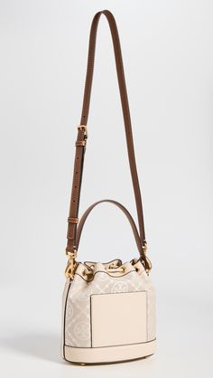 Find TORY BURCH T Monogram Bucket Bag on Editorialist. This Tory Burch bucket bag features a structured silhouette with gold-tone hardware. The bag is crafted from jacquard with a monogram pattern and leather trim. It has a drawstring top, patch interior pocket, and an optional adjustable strap. The bag is lined in suede and has a height of 8.25 inches, a length of 8.25 inches, and a depth of 4.75 inches. The strap drop is 21.75 inches and the handle drop is 4 inches. Monogram Canvas Pouch Shoulder Bag With Gold-tone Hardware, Monogram Canvas Bucket Bag With Detachable Handle, Everyday Bucket Bag In Monogram Canvas With Gold-tone Hardware, Everyday Monogram Canvas Bucket Bag With Gold-tone Hardware, Gold Bucket Bag With Top Handle And Gold-tone Hardware, Monogram Canvas Bucket Bag With Gold-tone Hardware, Designer Gold Bucket Bag With Detachable Handle, Luxury Bag In Monogram Canvas With Brass Hardware, Gold Monogram Canvas Shoulder Bag With Dust Bag