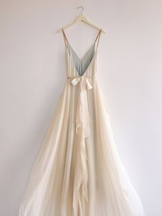 a dress hanging on a wall with a hanger in front of it that has a bow at the waist