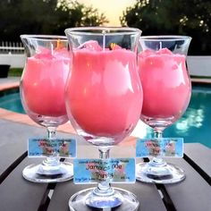 three glasses filled with pink liquid sitting on top of a table next to a pool