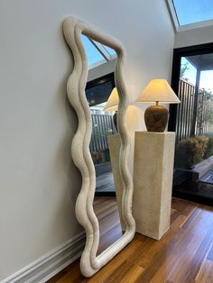 a large mirror sitting on top of a wooden floor next to a table with a lamp