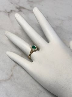 a woman's hand with a green ring on top of her left hand and a white marble background