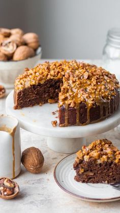 a chocolate cake with walnuts on top and one slice missing from it, sitting on a plate