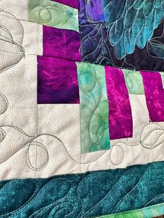 a close up view of a quilt on a table top with purple, green and blue strips