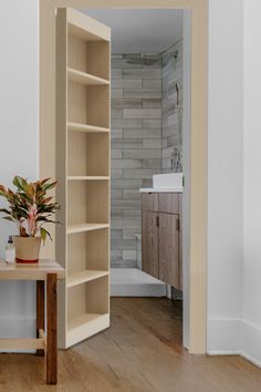 an open door leading to a bathroom with a plant in the corner and a sink