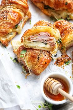 several pastries with meat and cheese on them next to a cup of honey syrup